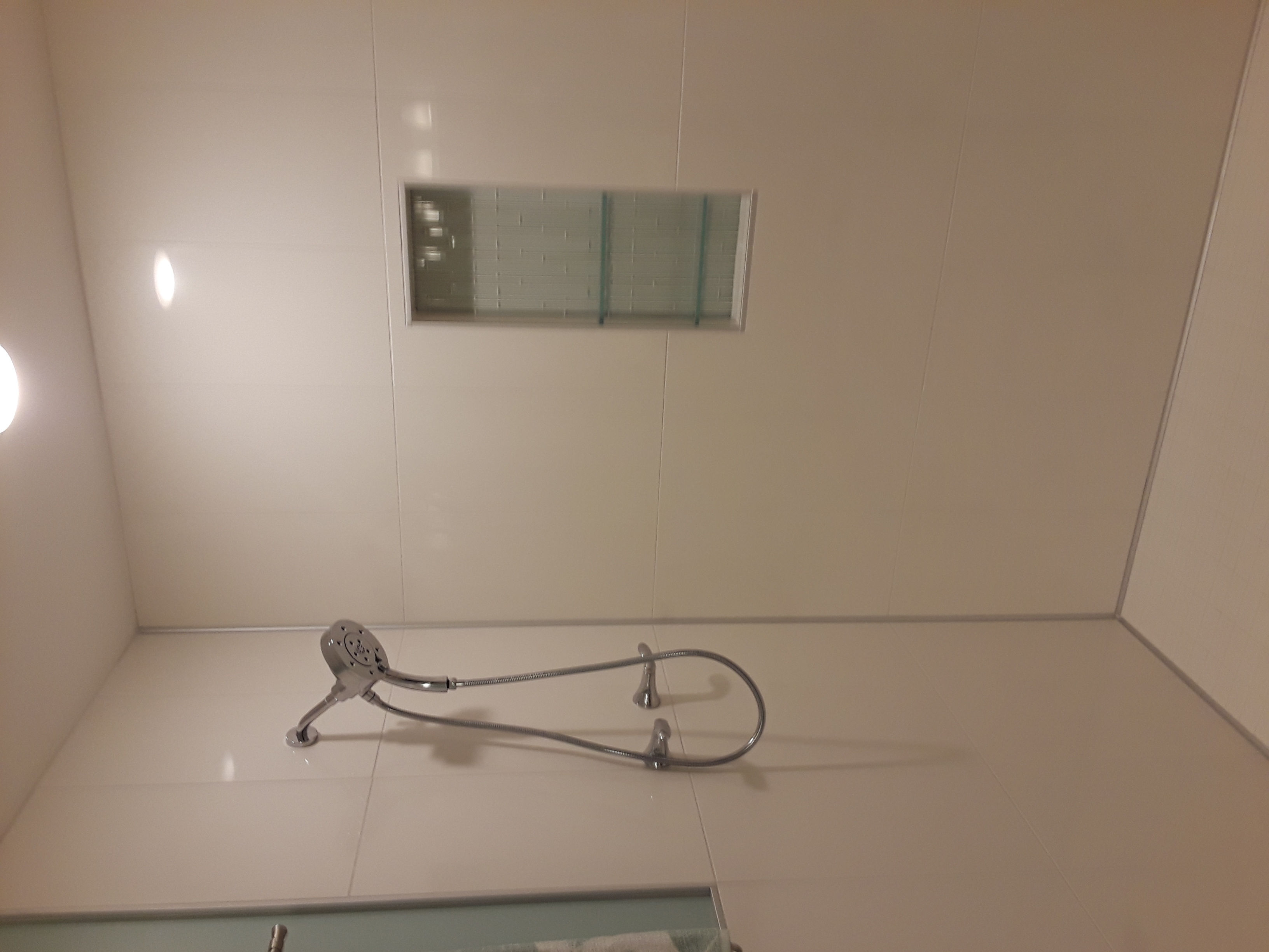 A white shower.  There is a flexible showerhead on the left, and a niche in the wall in the center of it.
